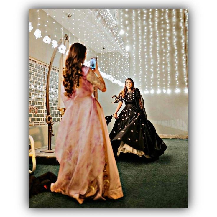 two women in long dresses are taking pictures with their cell phones while another woman sits on the floor