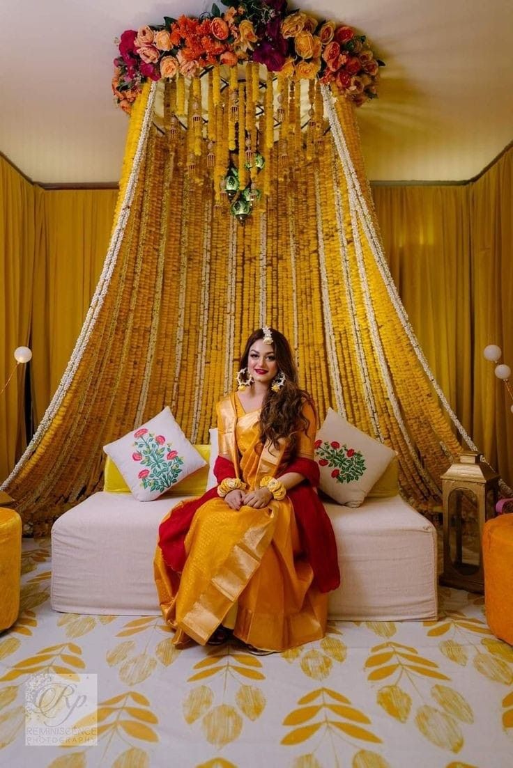 a woman sitting on top of a bed in front of a yellow drape covered wall