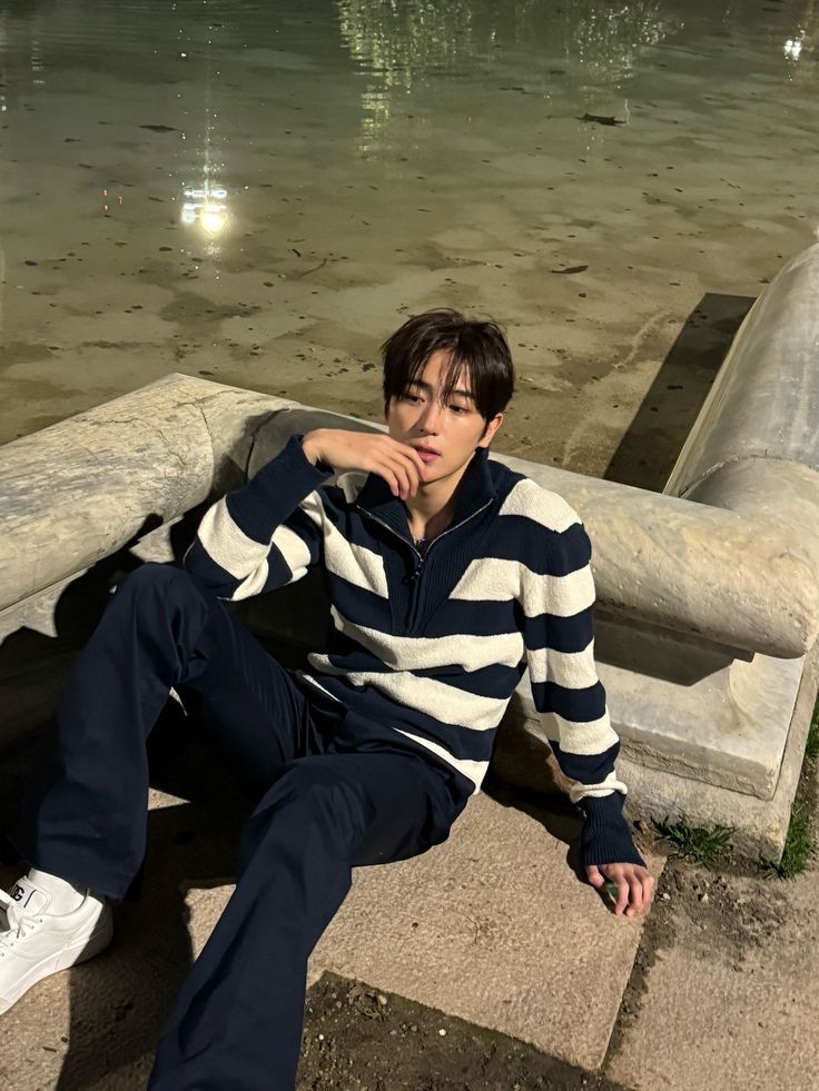 a young man sitting on top of a cement bench next to a pond with water