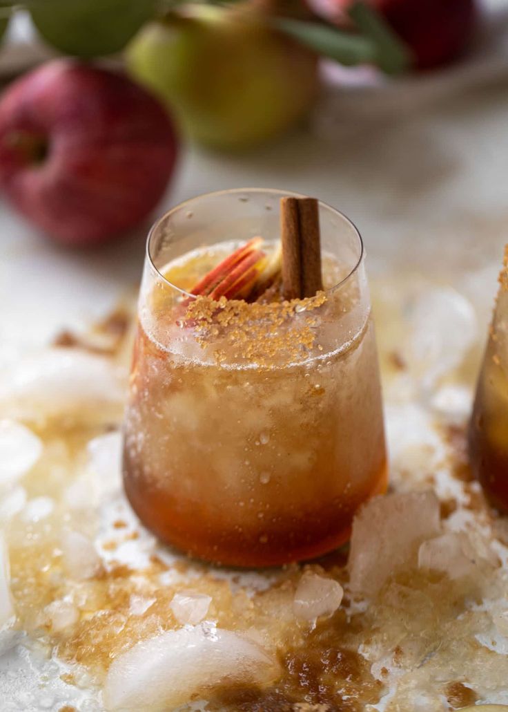 an apple cider cocktail with cinnamon sticks and ice on a table next to apples