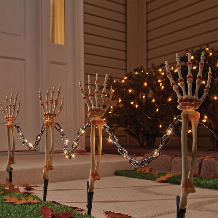 skeleton hand sculptures in front of a house with christmas lights on the trees behind them