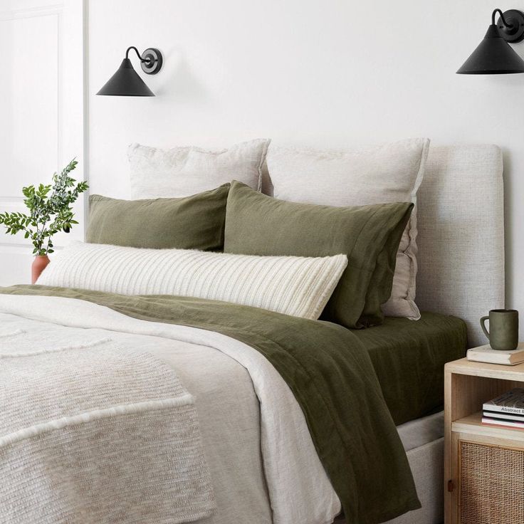 a bed with green sheets and pillows in a bedroom next to two black wall lights