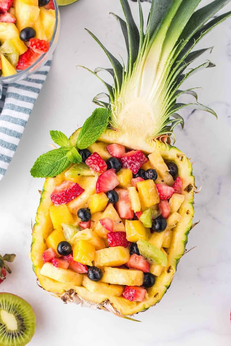 a pineapple fruit salad with strawberries and kiwis on the table next to it