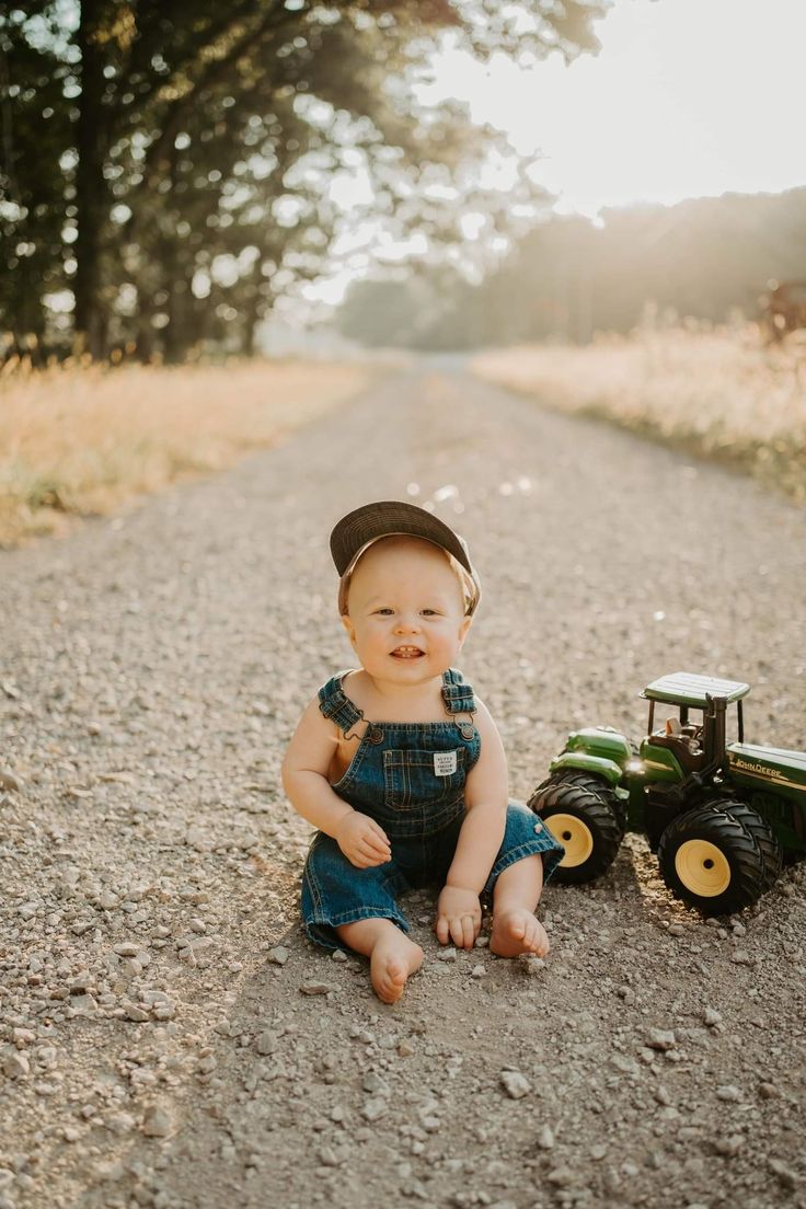 a baby sitting on the ground next to a toy tractor