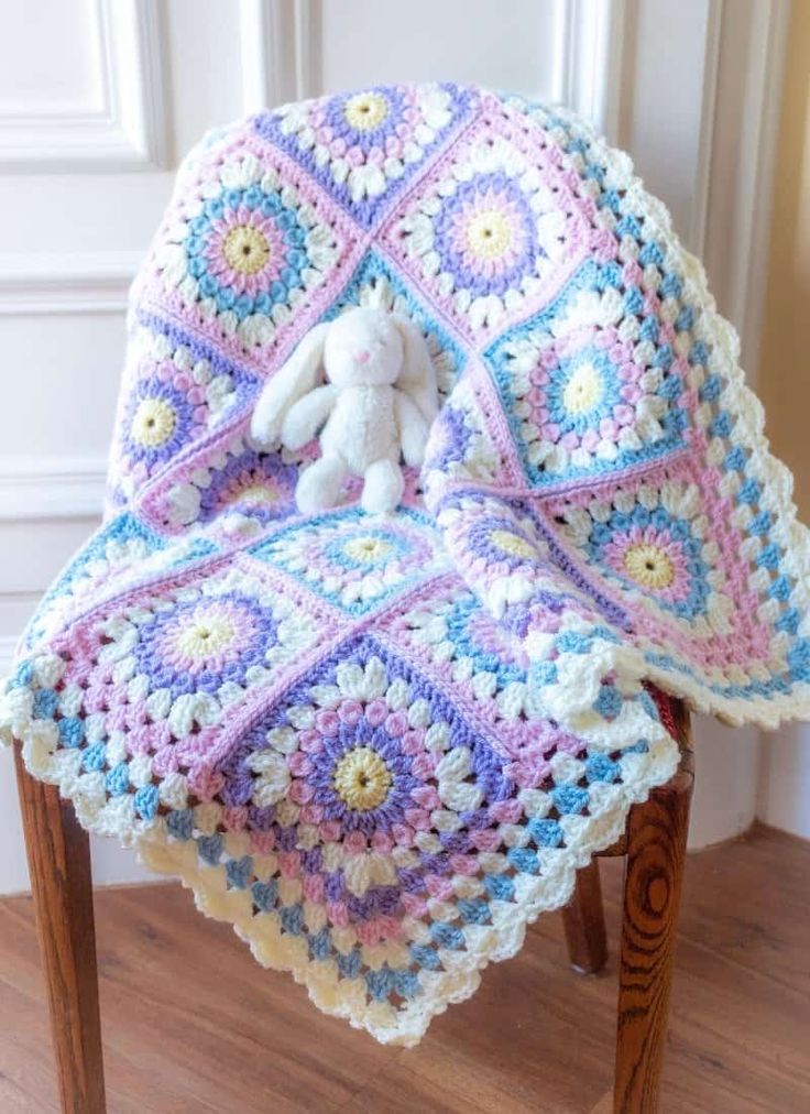 a crocheted blanket sitting on top of a wooden chair next to a stuffed animal