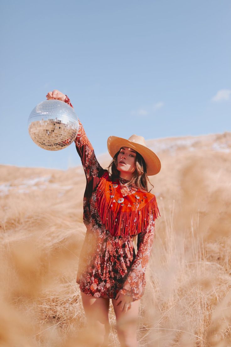 a woman in a cowboy hat is holding a silver ball and wearing a red dress