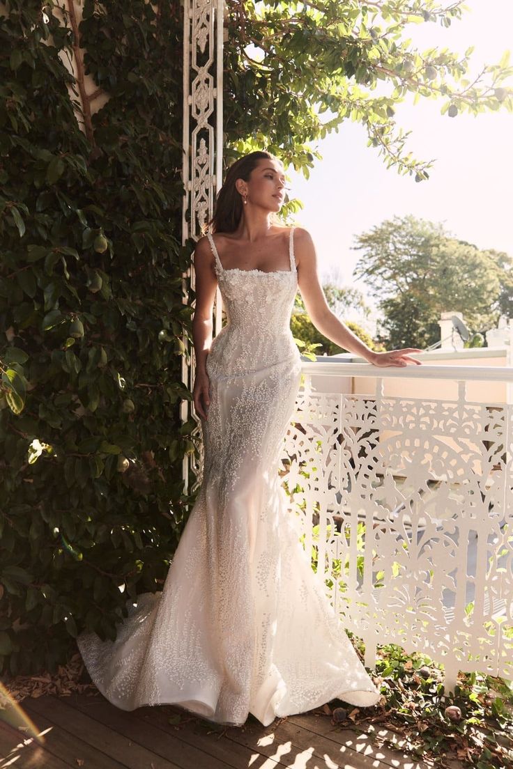 a woman in a wedding dress standing on a porch next to a white fence and trees