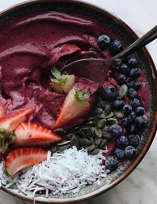 a bowl filled with blueberries, strawberries and coconut on top of a table