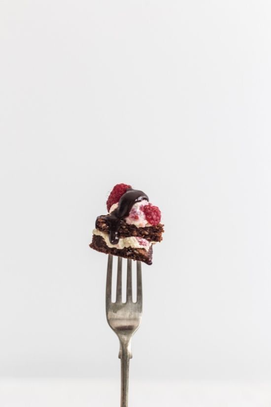 a piece of cake sitting on top of a fork with raspberries and chocolate