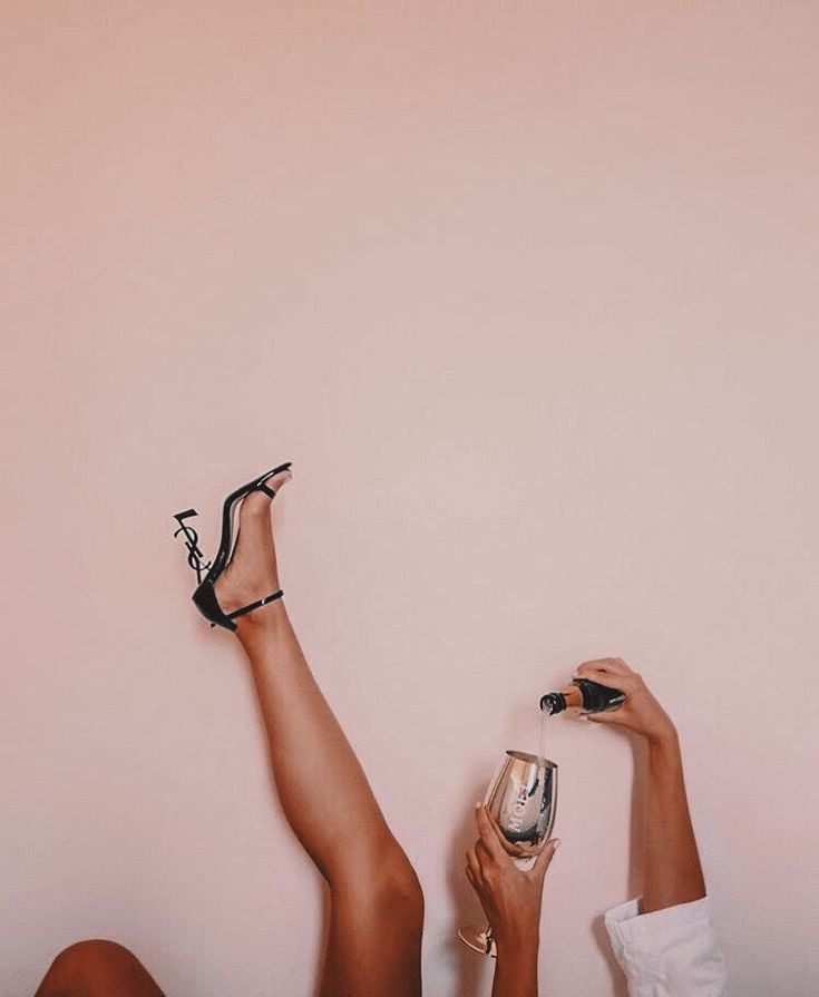 a woman laying on the floor with her legs up holding a wine glass and wearing high heels