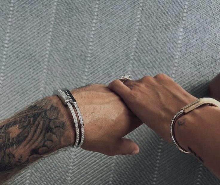 two people holding hands with tattoos on their arms and wristbands, both wearing matching bracelets