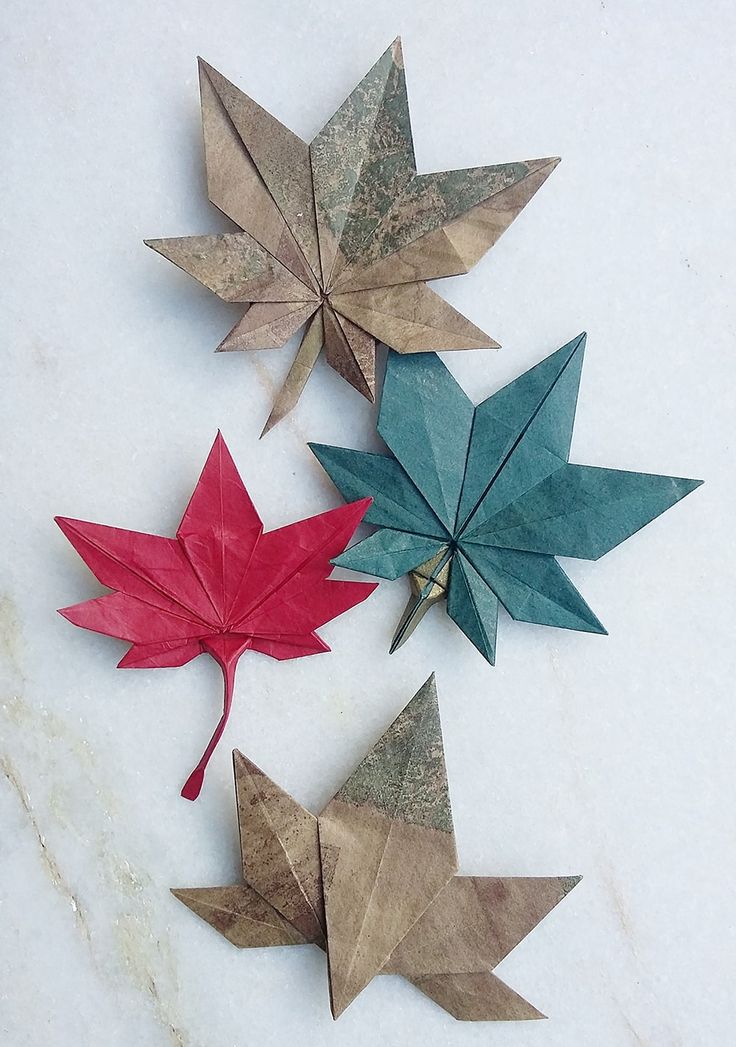 four origami maple leaves on a white marble countertop with red, green and blue ones