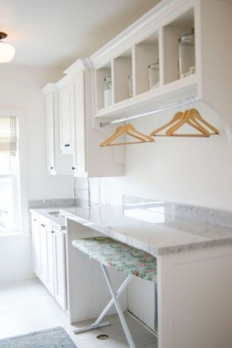 a kitchen with white cabinets and marble counter tops, along with an ironing board on the wall