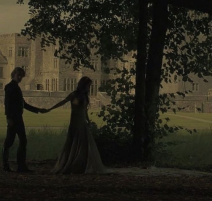 a man and woman holding hands in front of a large building with trees on the other side