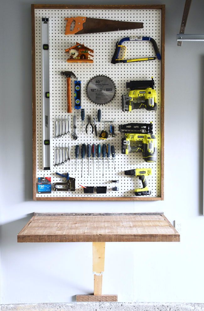 a pegboard with tools hanging on it in front of a wall mounted workbench