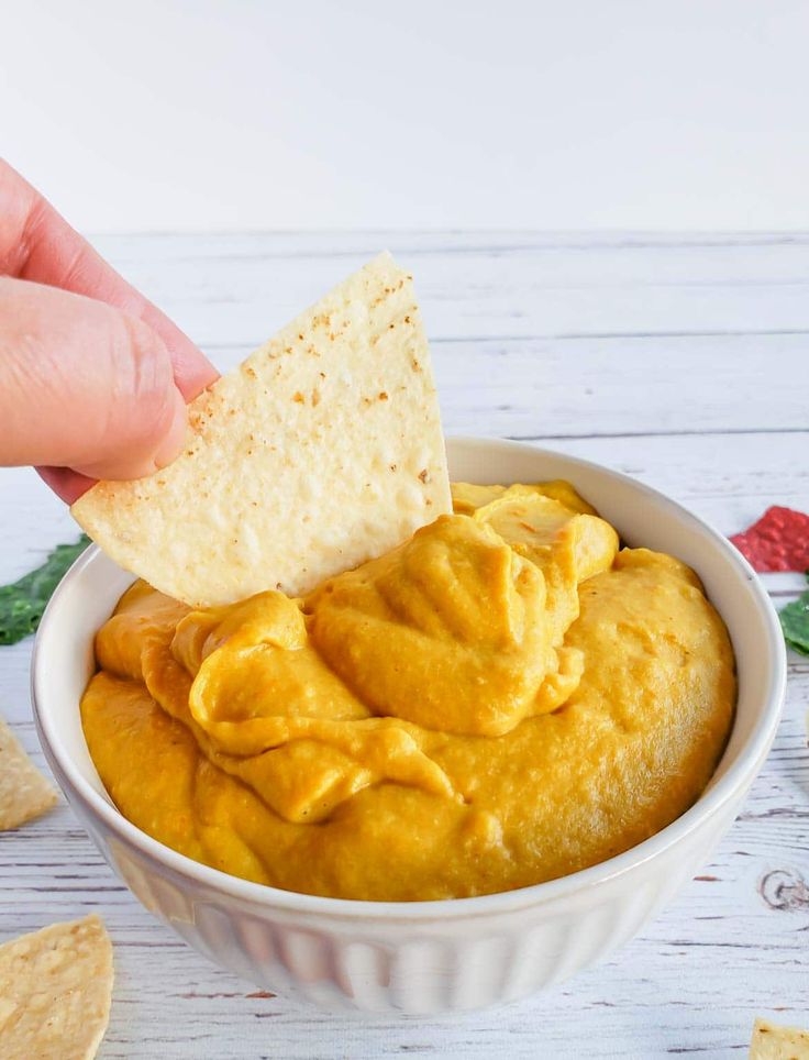 a hand dipping a tortilla chip into a bowl of hummus