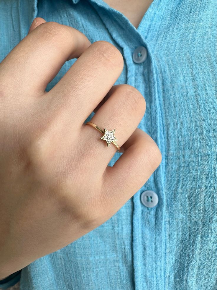 a woman's hand wearing a gold ring with a star on the middle, and a diamond in the middle