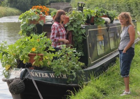 two women standing on the side of a boat filled with plants