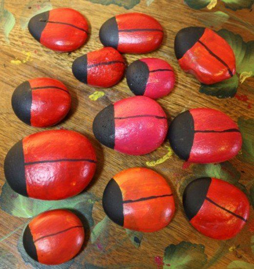 some red and black painted rocks on a wooden table with leaves around them in the shape of ladybugs