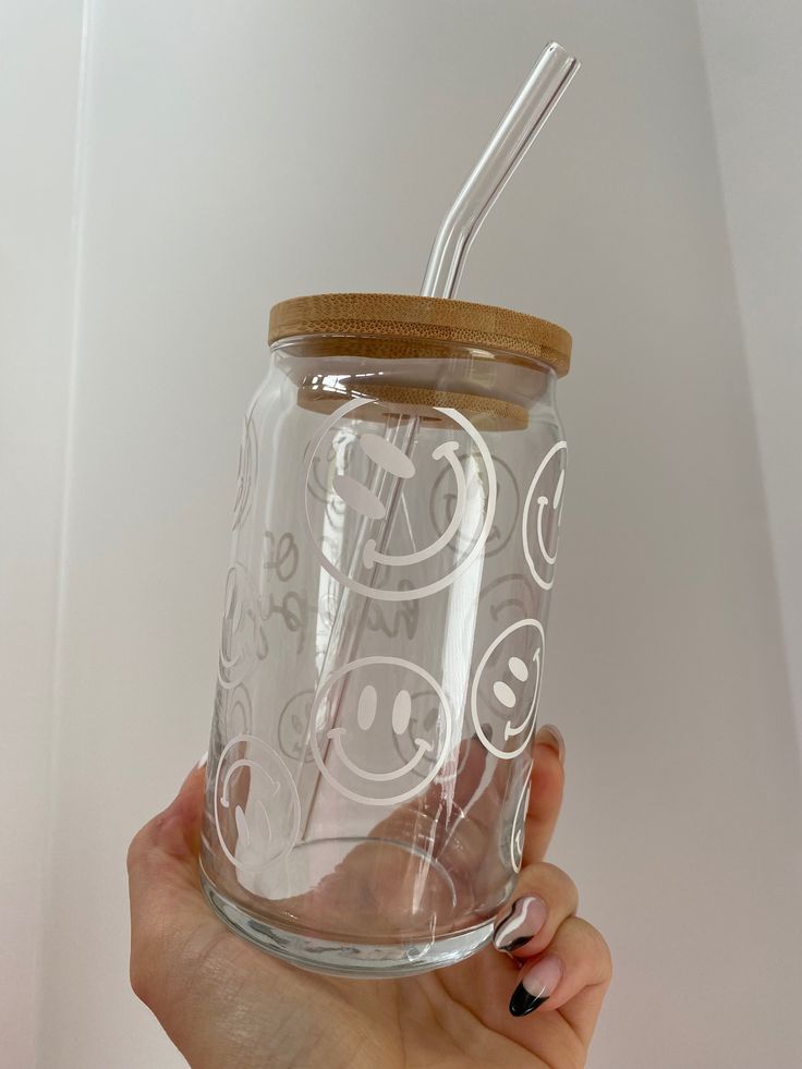 a person holding a glass jar with a straw in it and smiley faces on the lid