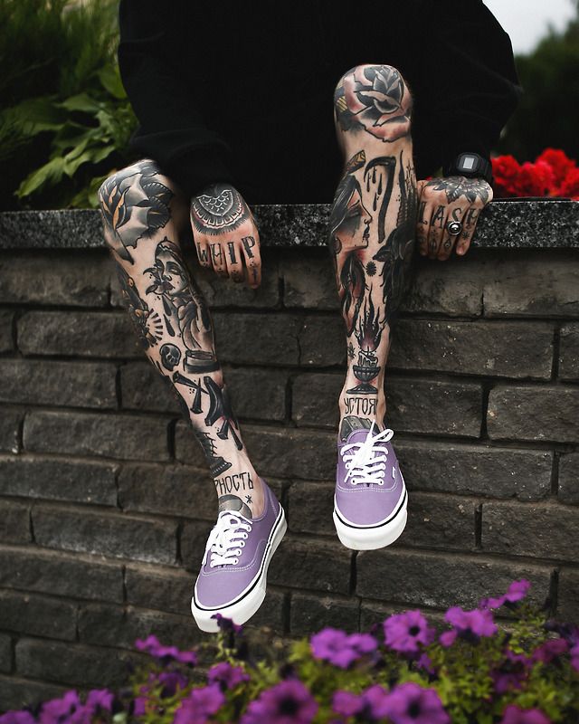 a man with tattoos sitting on top of a brick wall next to flowers and plants