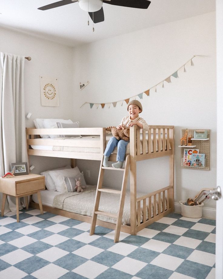 a little boy sitting on top of a bunk bed in a room with blue and white checkered flooring