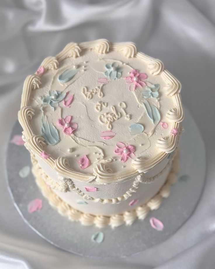 a white cake with pink and blue frosting on a silver platter next to a white cloth