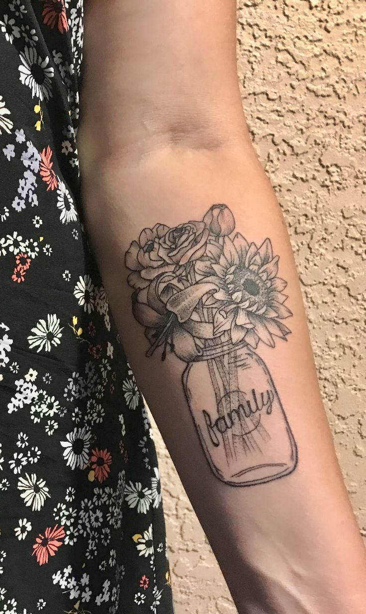 a person with a tattoo on their arm holding a mason jar filled with sunflowers