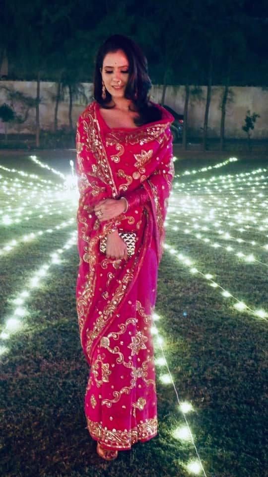 a woman in a red sari is standing on the grass with lights behind her