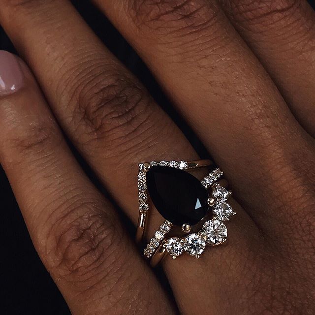 a woman's hand with a ring on top of her finger and an oval shaped black diamond in the middle