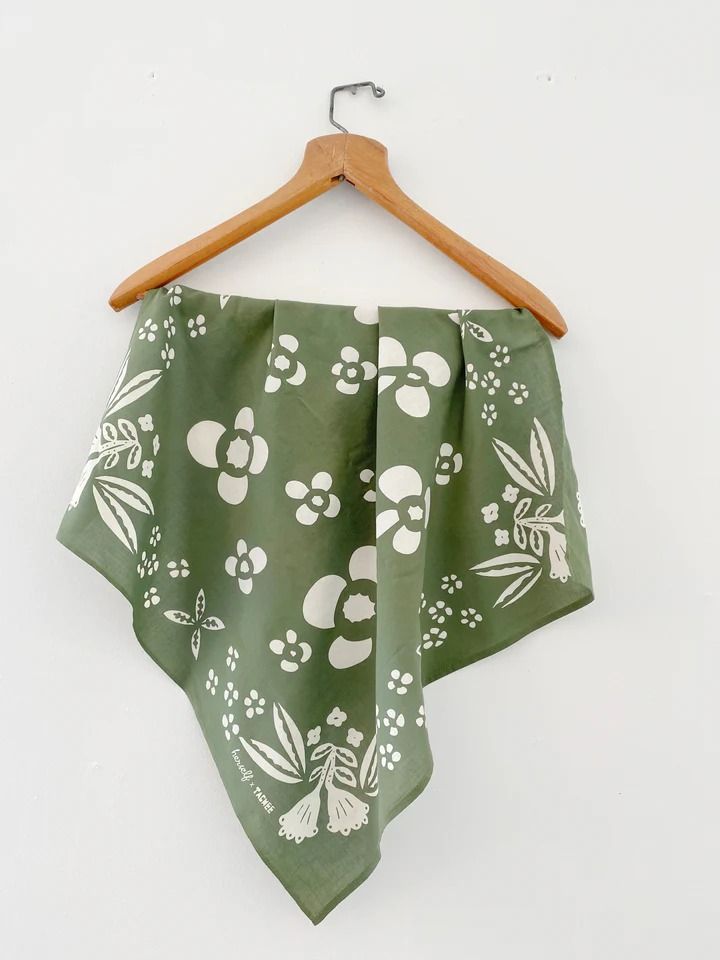 a green bandana with white flowers and leaves on it hanging from a wooden hanger