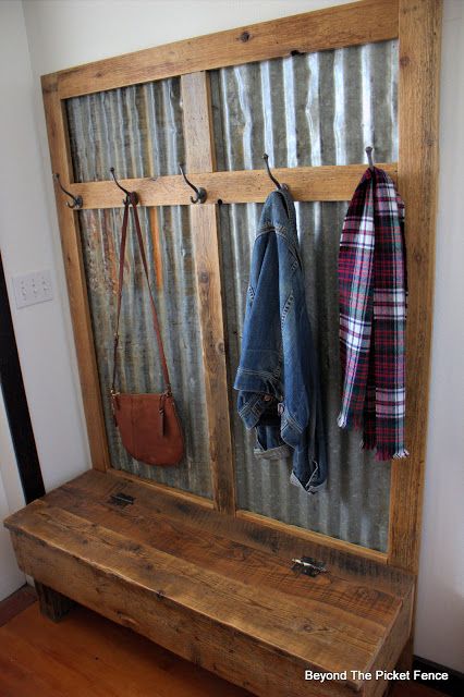 a wooden bench sitting next to a metal wall mounted coat rack with two coats hanging on it