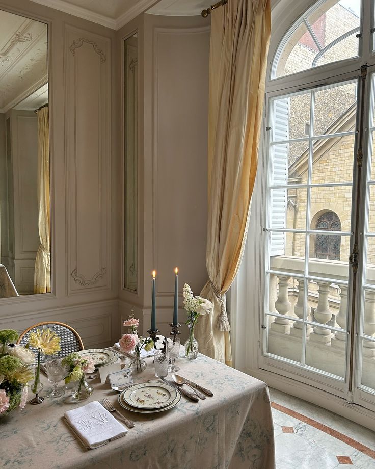 a dining room table is set with flowers and candles for an elegant dinner party in front of a large window