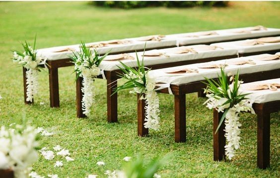 a row of wooden benches sitting on top of a lush green field covered in white flowers