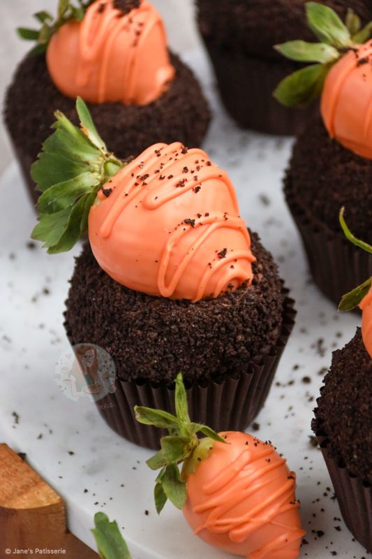 chocolate cupcakes with orange frosting and strawberries on top are sitting on a white plate