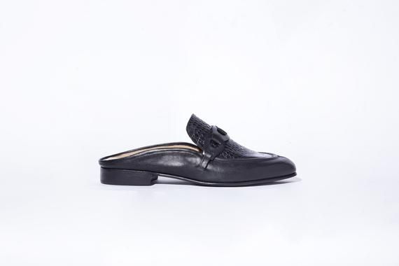 The Pilar Mule is the backless sister style to the Pilar loafer featuring a leather-link chain and corded seam detail with a contrasting black croc-embossed leather vamp and square toe. Upper is crafted from black vegetable tanned leather. Tinted leather sole and stacked heel measuring 18mm and a memory foam-cushioned insole.  Handmade in Argentina. Style the Pilar Mule with sporty and refined pieces (like joggers, a bandeau top and a blazer) for an interesting contrast for play, or with loose t Luxury Slip-on Mules For Work, Elegant Mules With Textured Sole, Elegant Textured Sole Mules For Work, Elegant Workwear Mules With Textured Sole, Workwear Mules With Textured Sole, Formal Leather Mules With Textured Sole, Formal Mules With Textured Sole, Elegant Leather Mules For Work, Luxury Leather Mules For Work