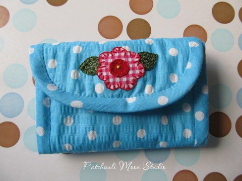 a blue purse with a flower on it sitting on a polka dot tablecloth background