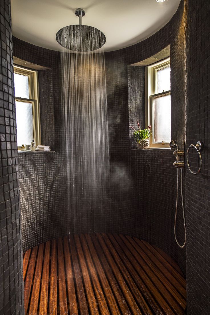 a shower head in the middle of a wooden floored room with two windows above it