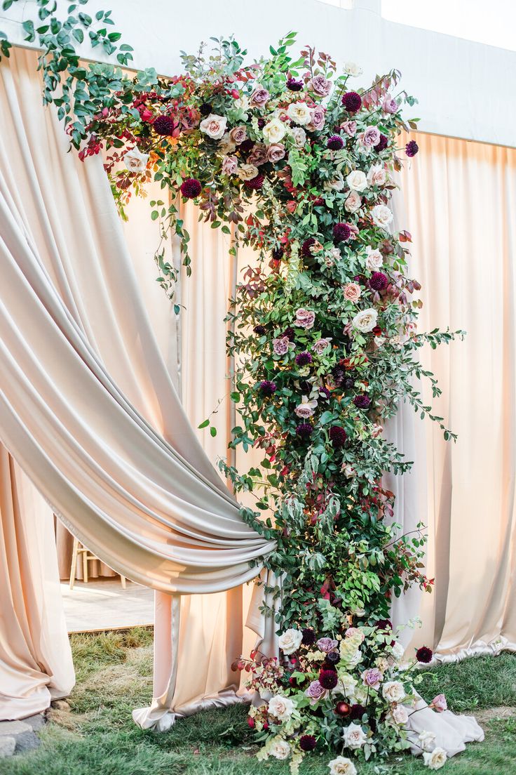 an arch covered in flowers and greenery next to a drapeed curtain at a wedding