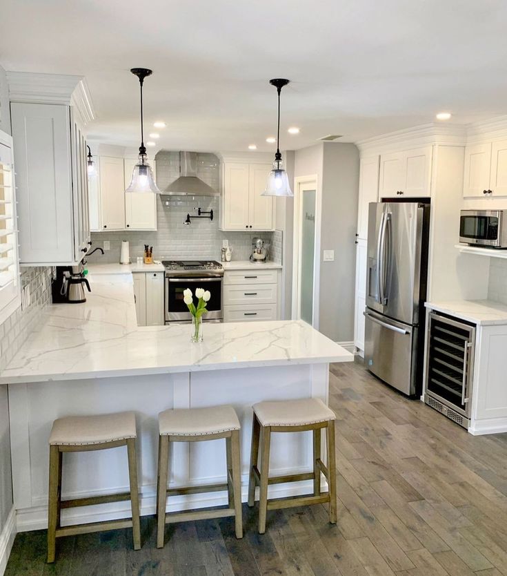 a large kitchen with white cabinets and marble counter tops, two stools are in front of the center island