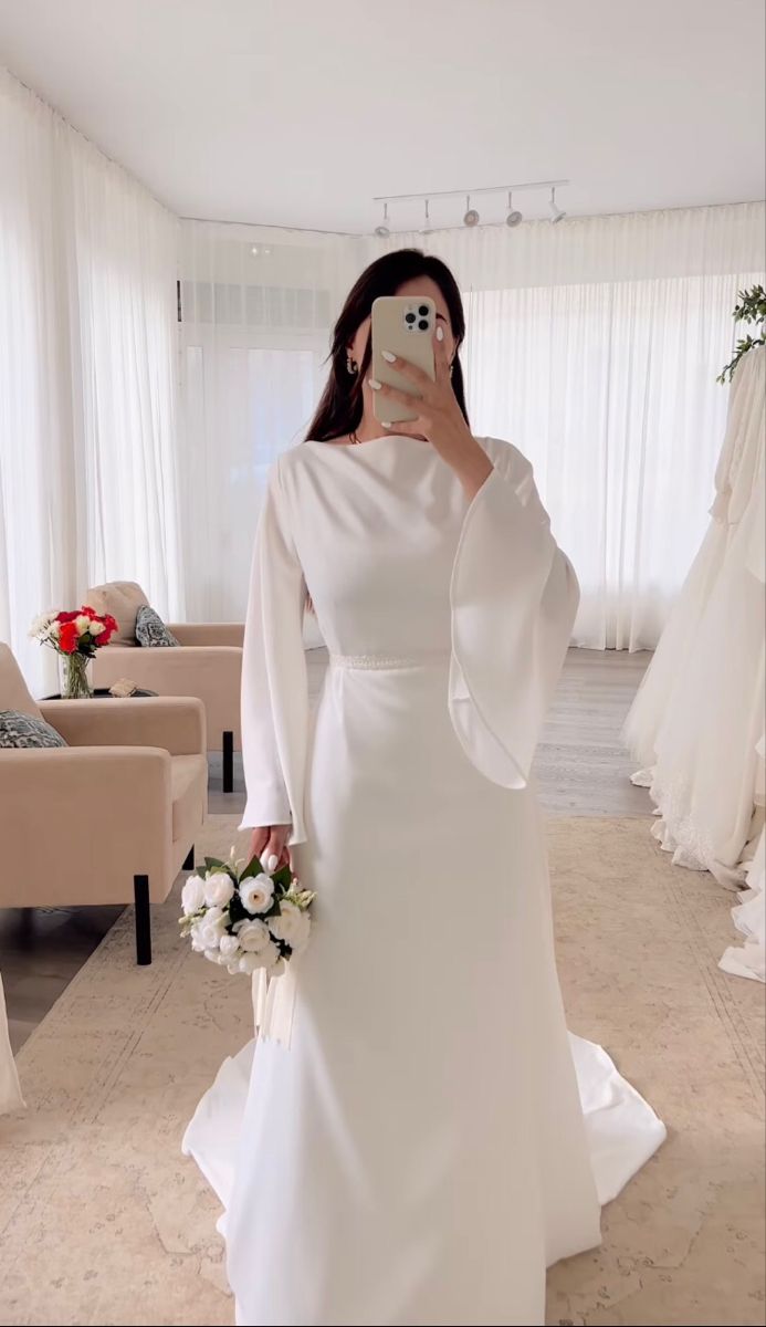 a woman in a white dress taking a selfie with her cell phone while wearing a wedding gown