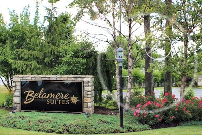 a welcome sign in front of some trees and flowers on the side of the road