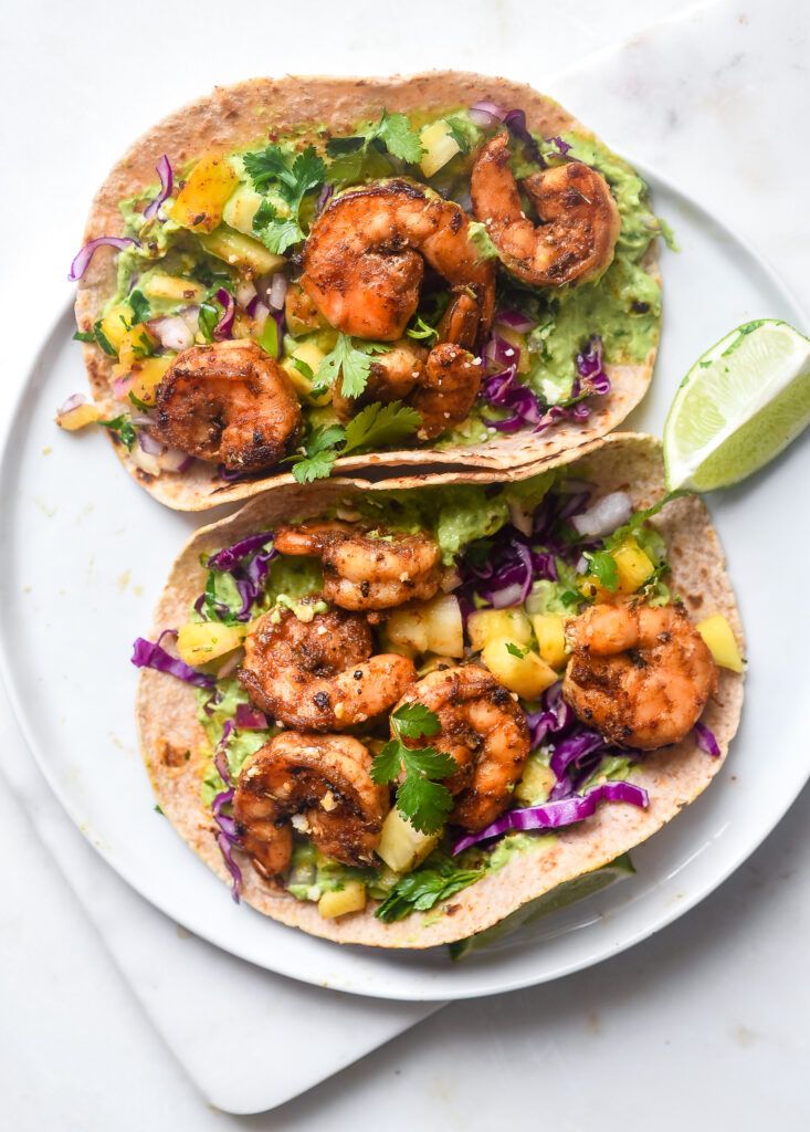 three tacos with shrimp, avocado and cilantro on a blue plate