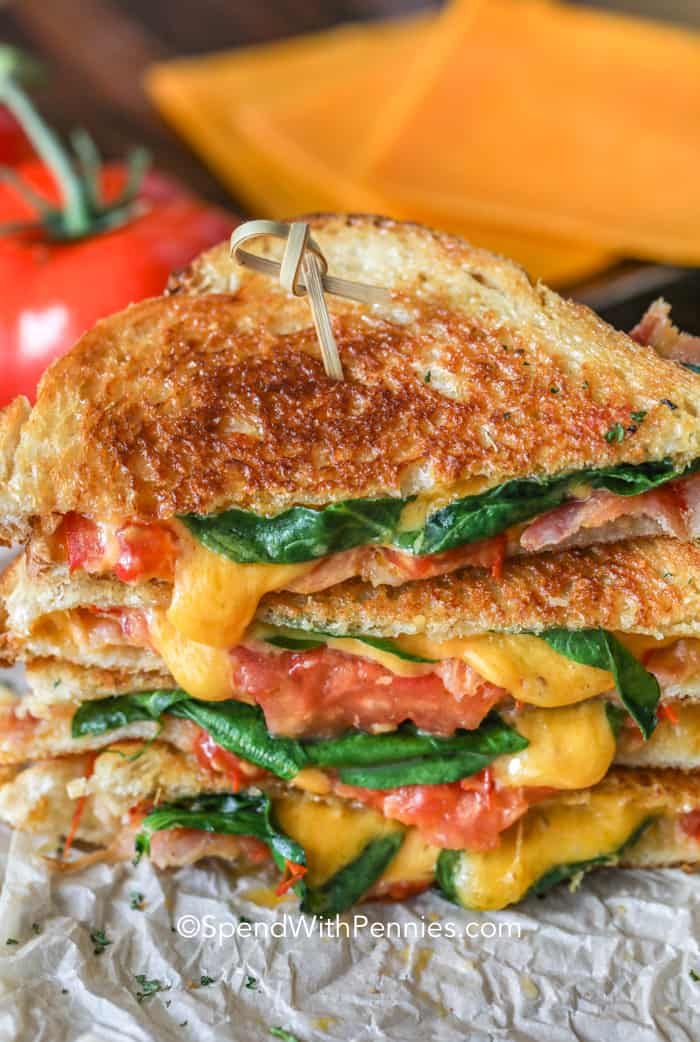 a grilled cheese and tomato sandwich is stacked on top of foil with tomatoes in the background