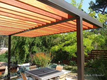 an outdoor dining table and chairs under a pergolated roof in a backyard area