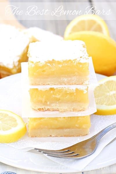 lemon bars stacked on top of each other on a plate next to sliced lemons