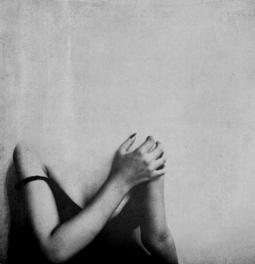 a black and white photo of a woman with her hands on her face, in front of a wall