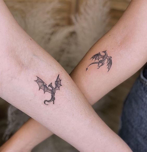 two people with tattoos on their arms holding each other's hands and one has a dragon tattoo on it