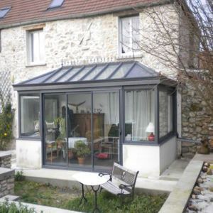 a patio with a table and chairs in front of a stone building that has a glass door