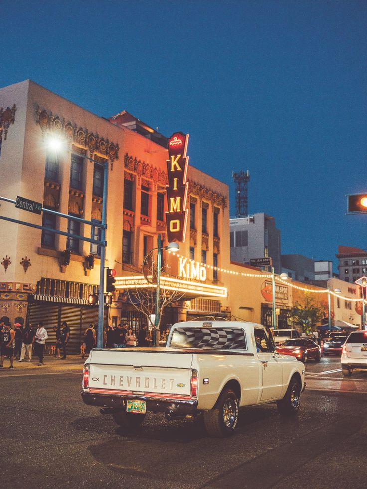 an old pickup truck is parked in front of a movie theater on the street at night